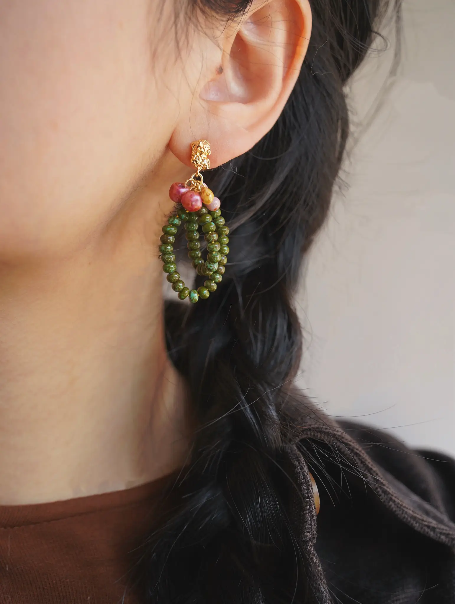 A model wearing botanical drop earrings with gold studs and layered green beaded loops.