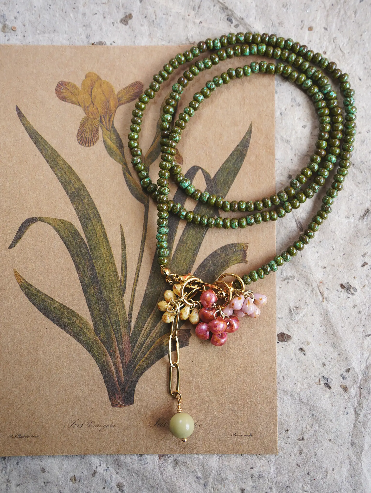 A long botanical sweater chain with green glass beads coiled on a vintage floral card.