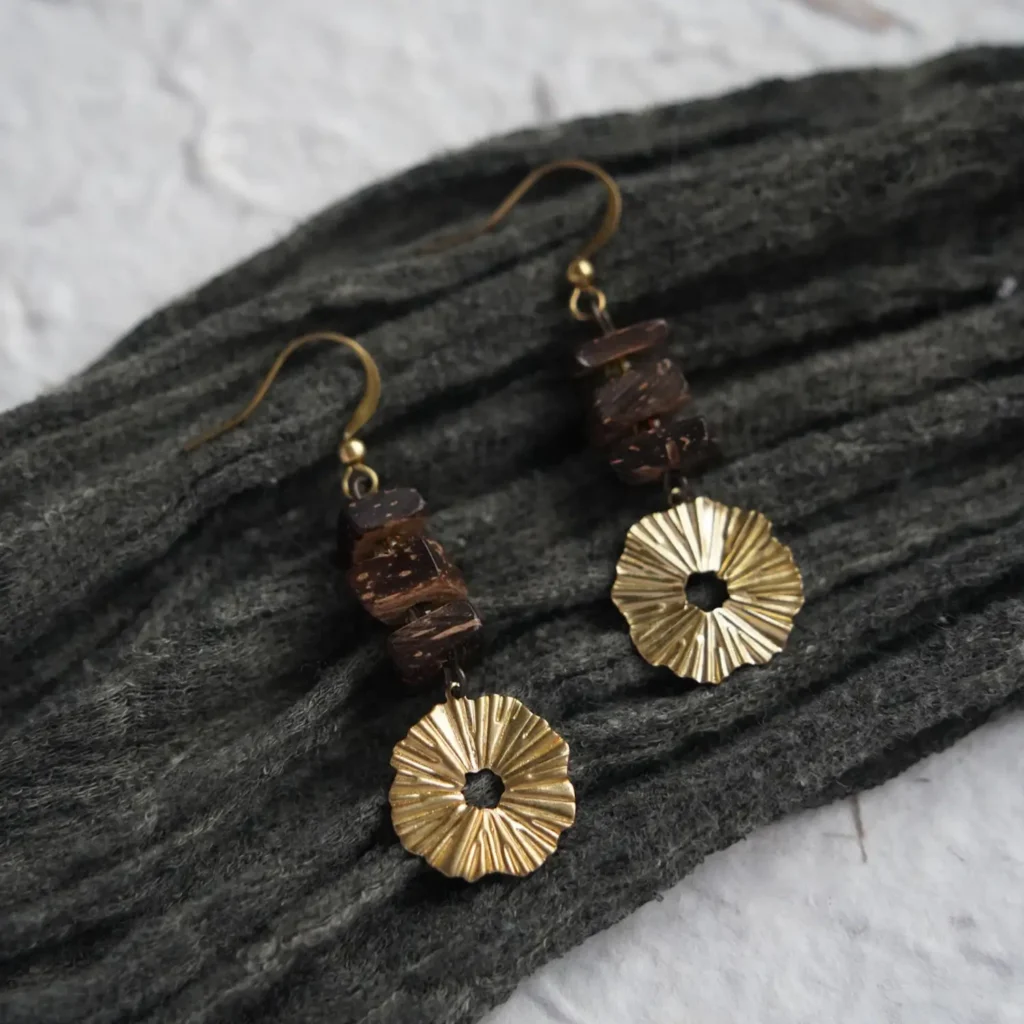 Geometric coconut wood earrings with pleated brass discs resting on a dark textured fabric.