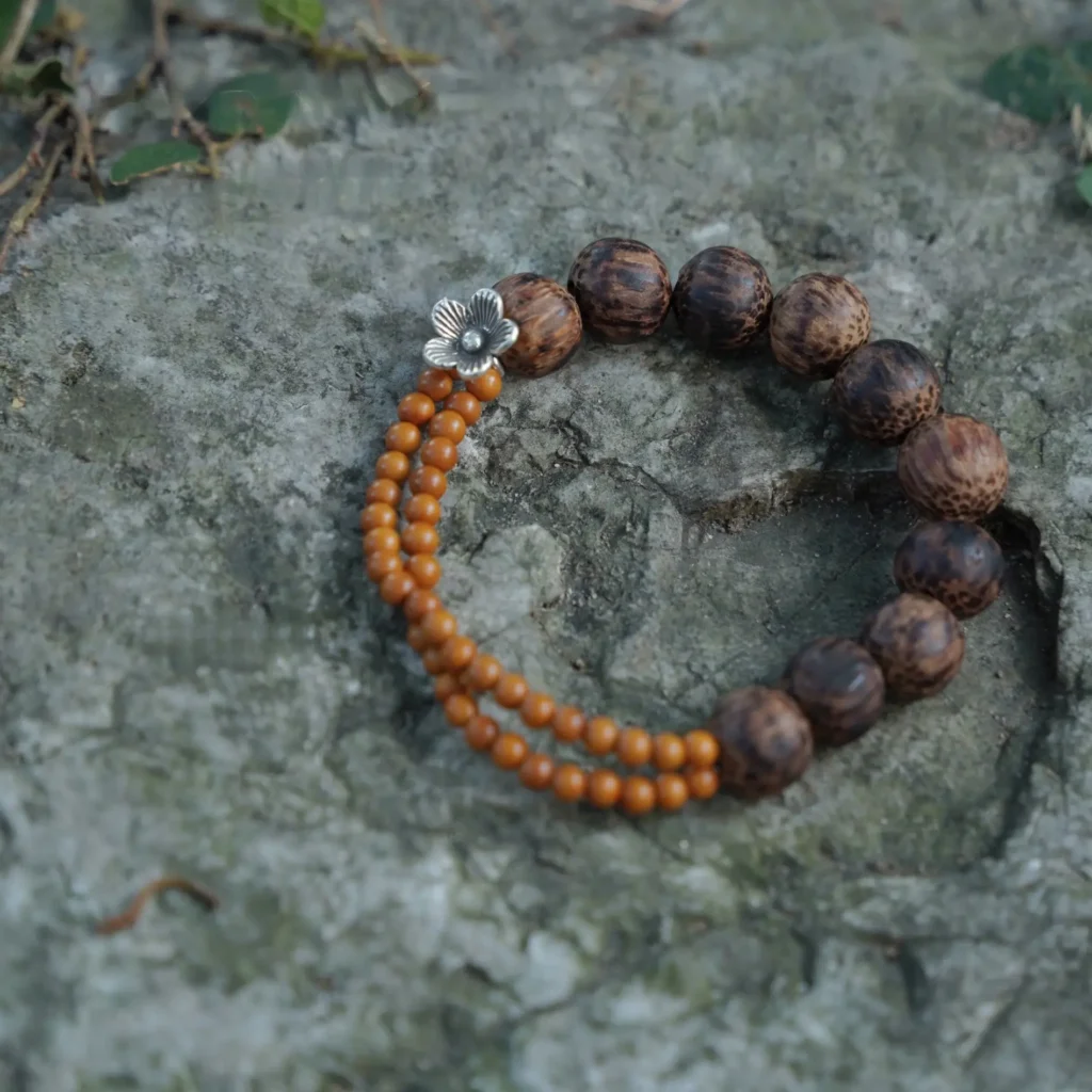 A coconut wood and olive pit beaded bracelet with a silver flower resting on a gray rock.