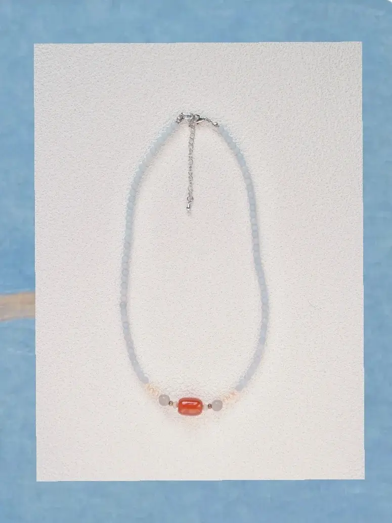 An oval-shaped beaded necklace centered flat on a white surface, framed by a soft blue outer border.