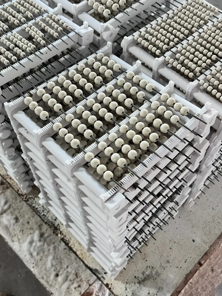 Rows of clay beads drying on fine metal wires stacked neatly on white racks.