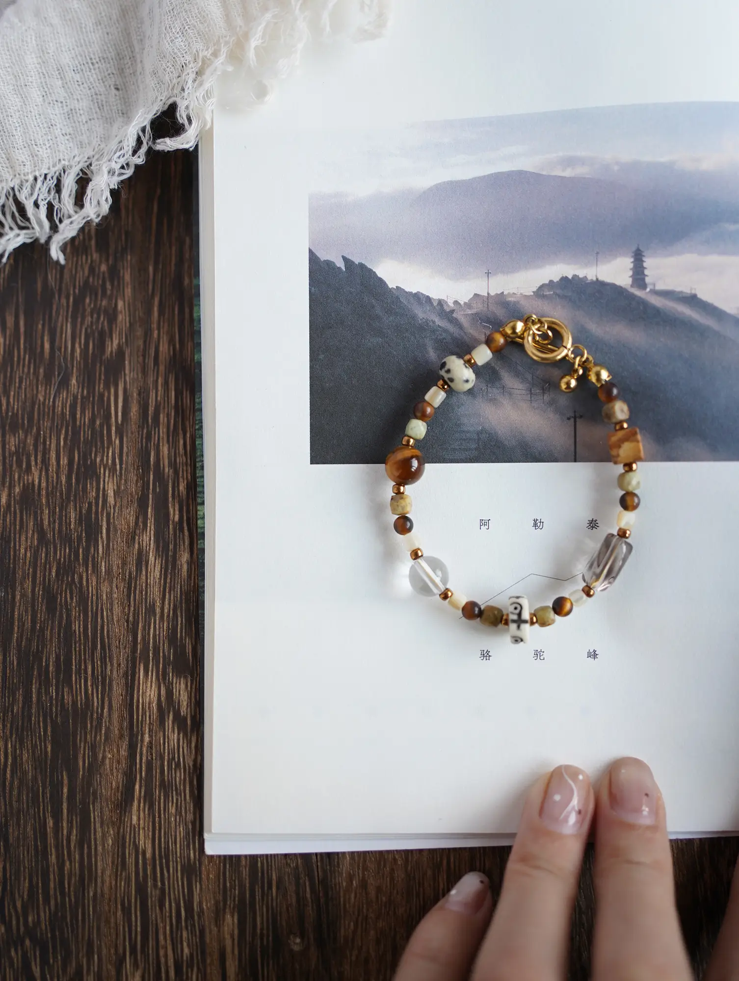 Earthy gemstone bracelet on an open book featuring a mountain landscape background.