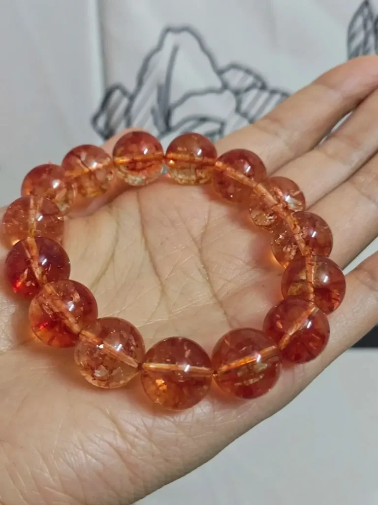 A hand holding an imitation bracelet made of reddish-orange translucent glass beads.