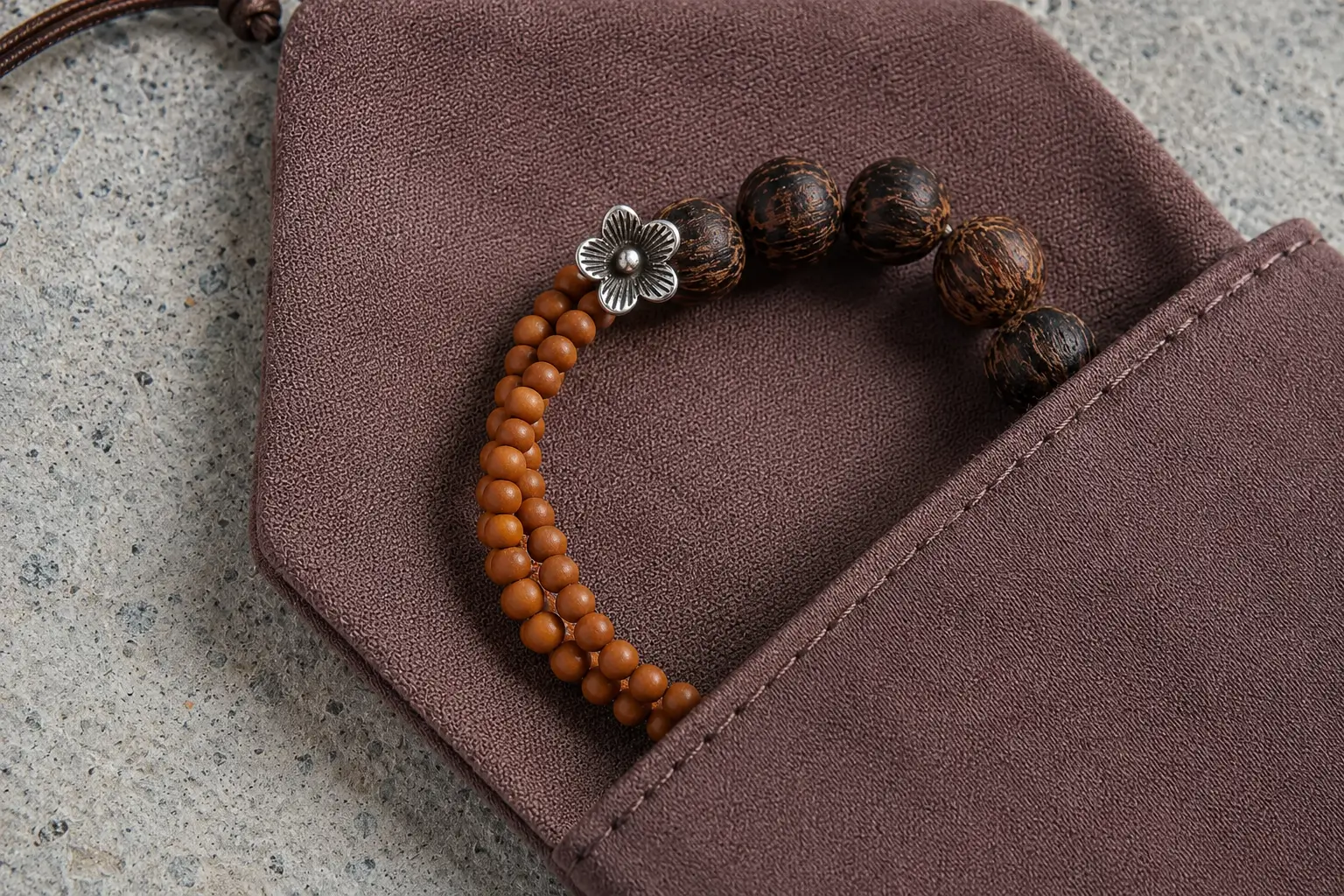 A coconut wood bracelet resting inside a mauve jewelry pouch on a gray concrete surface.