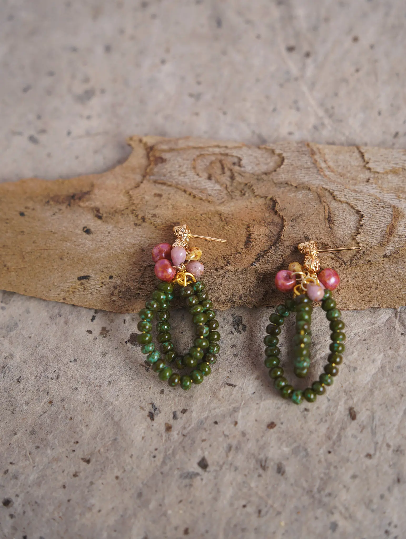 A pair of beaded earrings with shiny gold-plated silver posts resting on a piece of natural wood bark.