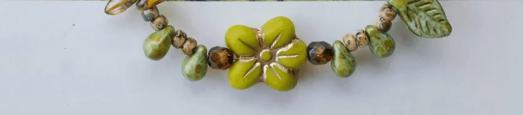 Close-up of green Czech glass flower bead with gold-wash detailing on recessed grooves.