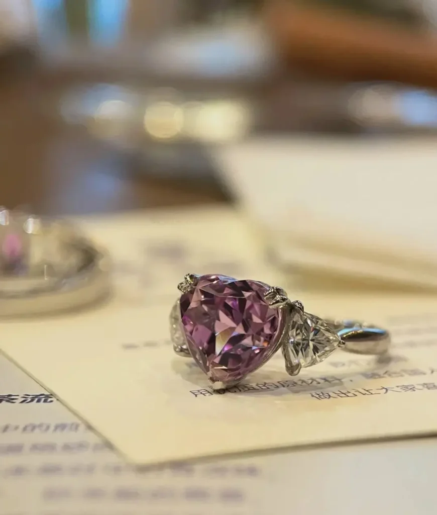 A heart-shaped pink kunzite ring flanked by two triangular diamonds on a platinum band.