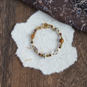 Handmade earthy gemstone bracelet on textured paper and wood surface.