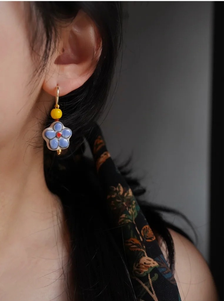 Close-up profile of a woman wearing a blue ceramic flower hoop earring with a yellow accent bead.