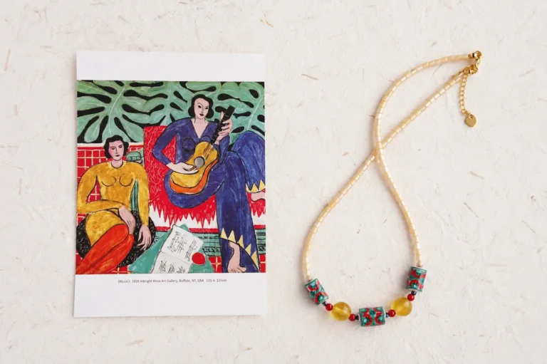 A hand-painted ceramic necklace next to a Matisse La Musique art print on texturized paper.