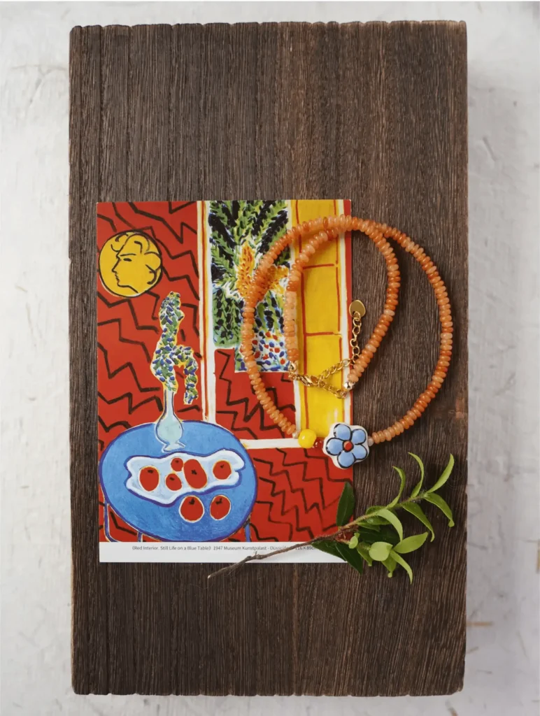 Red aventurine bead necklace draped over a Matisse postcard print on a dark wood board.