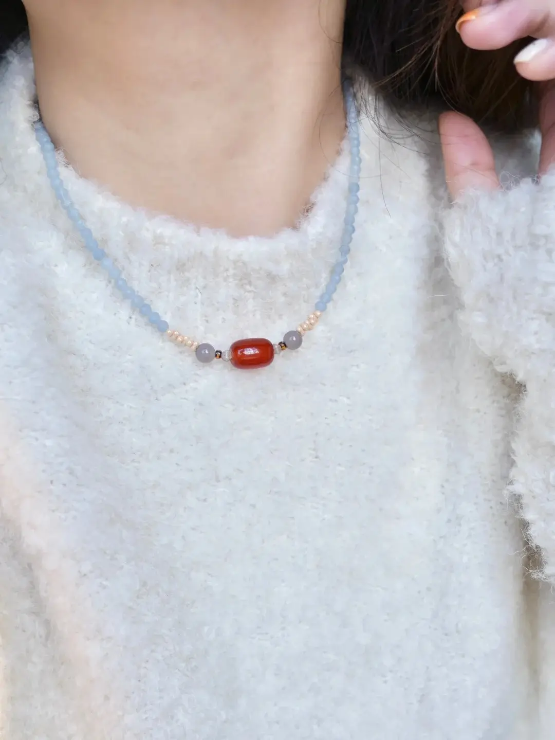 Close-up of a blue gemstone necklace resting on a person's collarbone over a white sweater.