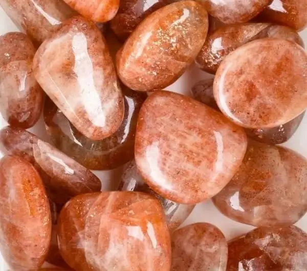 Polished, smooth orange sunstone tumbled crystals showing faint internal metallic copper shimmers.