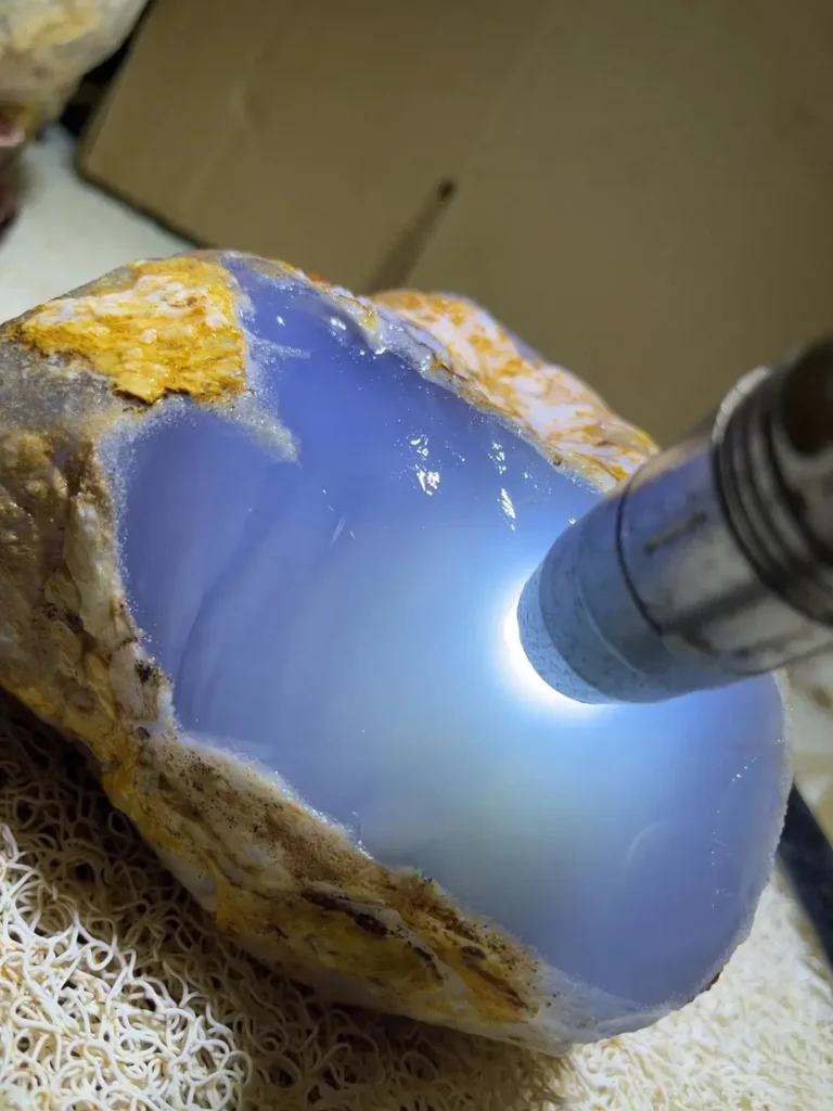 Flashlight illuminating a raw blue chalcedony stone, showing its translucent waxy luster.