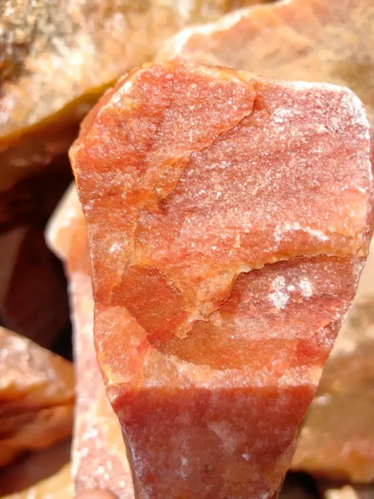 Close-up of raw red aventurine rough stone with a textured, unpolished surface showing natural orange-red tones.