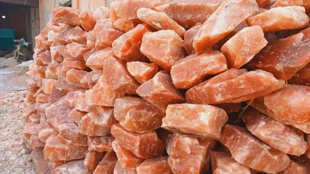 A large pile of rough, unpolished orange-pink sunstone mineral rocks stacked outdoors.