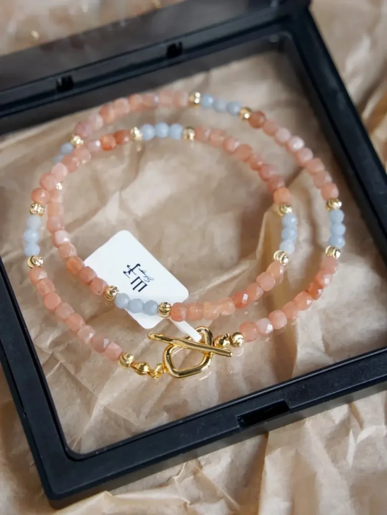A single beaded necklace with orange sunstone and blue accents coiled inside a black display box.