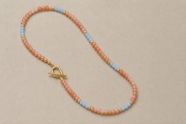A beaded necklace with peach sunstone, light blue accents, and a gold clasp on a gray background.