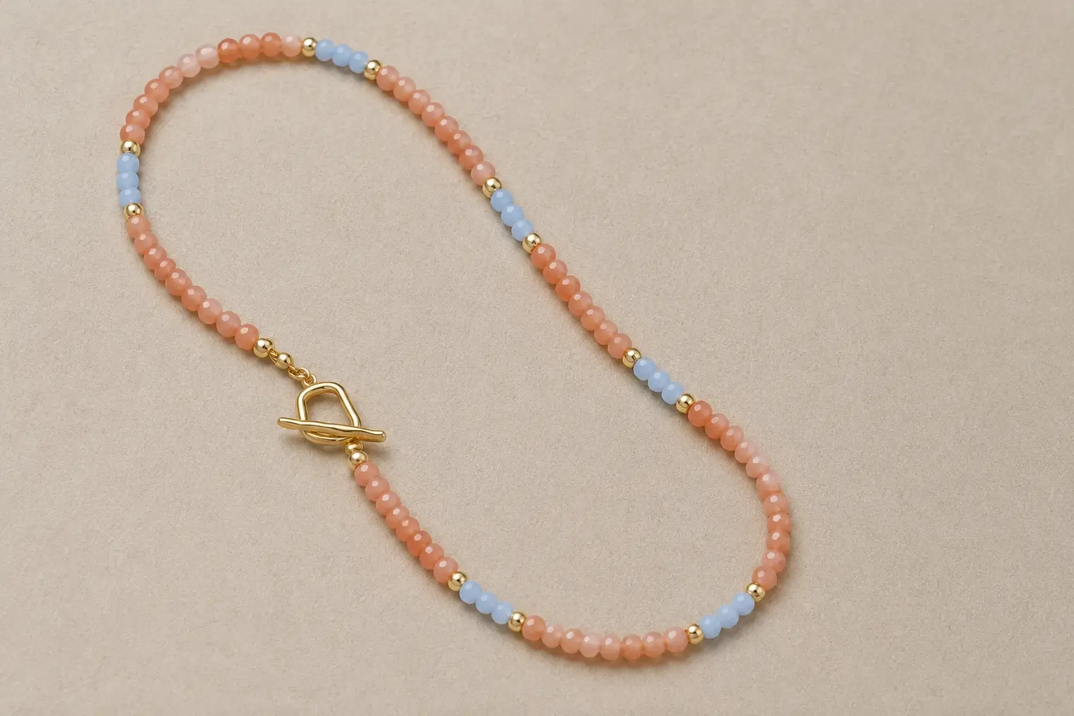 A beaded necklace with peach sunstone, light blue accents, and a gold clasp on a gray background.