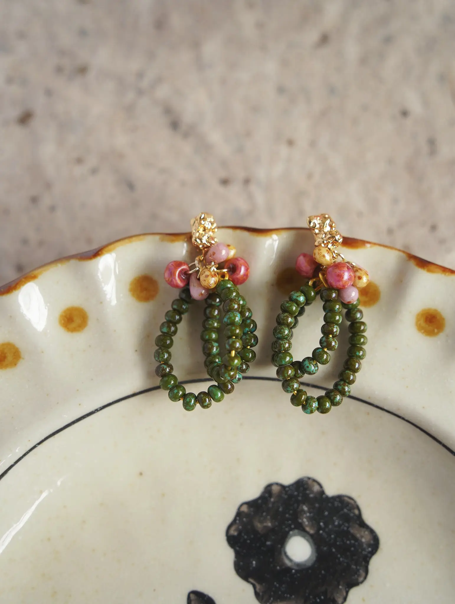 A pair of vintage green glass earrings resting on the rim of a speckled ceramic dish.
