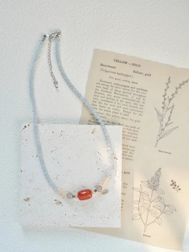 Beaded gemstone necklace laid over a textured limestone tile and an antique botanical print.