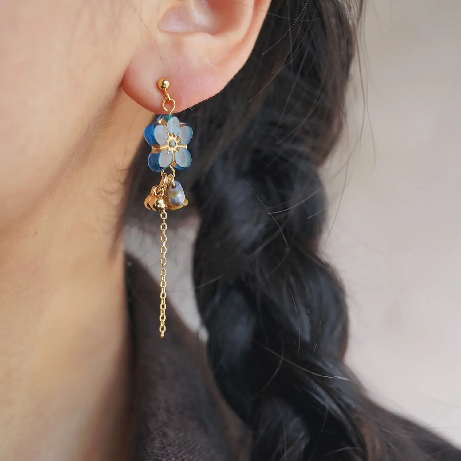 Woman wearing a handmade blue glass earring with a dark top, showing the jewelry detail.