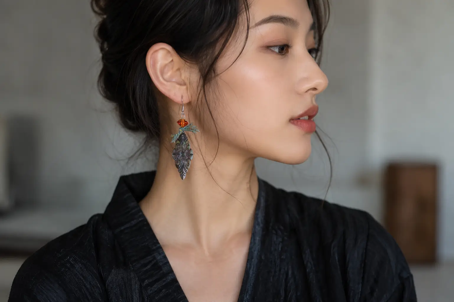 A woman in profile wearing a carved black mother-of-pearl earring with an orange bead.