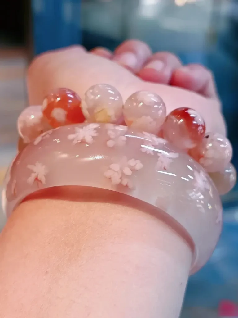 Translucent cherry blossom agate bangle and beaded bracelet worn on a wrist showing floral inclusions.