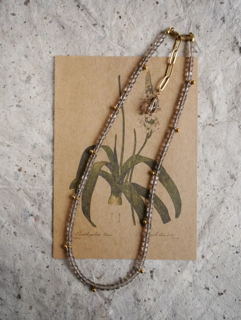 A long handmade natural gemstone necklace with a gold titanium chain displayed on paper.