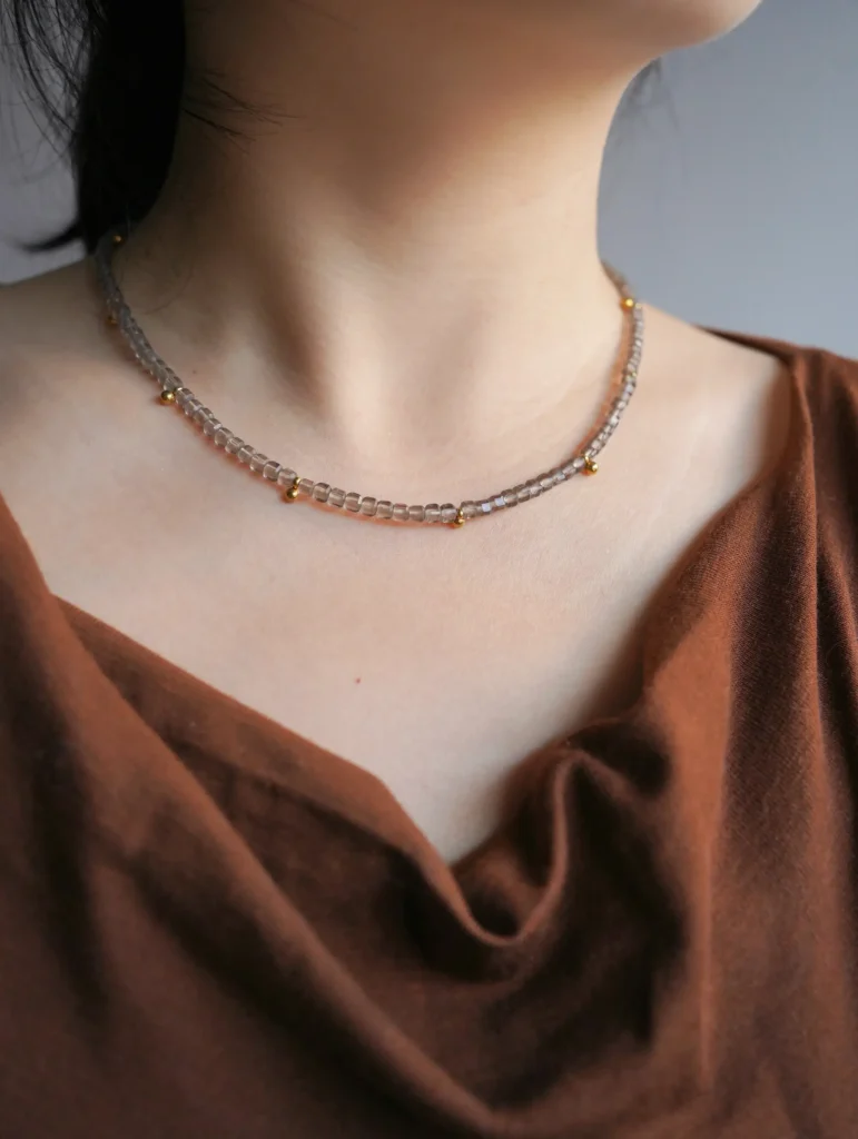 A woman wearing a faceted gray-brown natural stone choker necklace with gold beads.