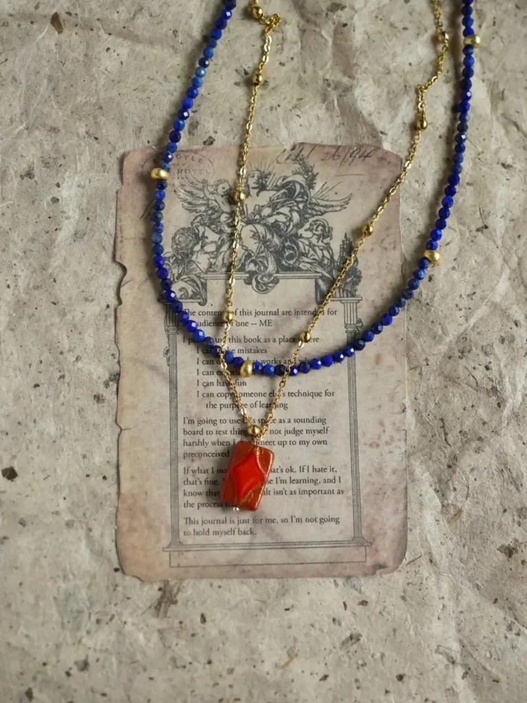 Faceted lapis lazuli beads layered with a gold pendant chain on vintage paper.