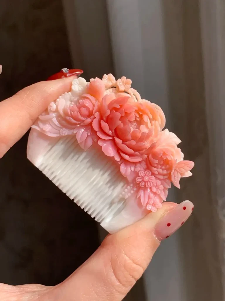 Hand-carved Queen Conch shell comb with pink floral relief and white shell teeth.