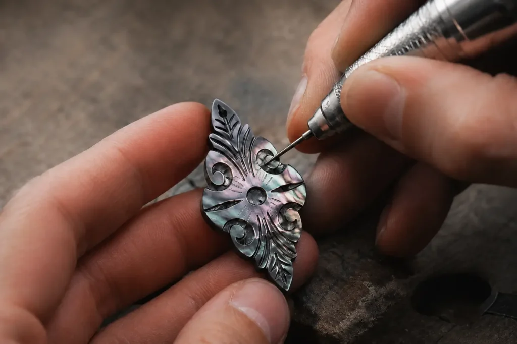 An artisan uses a rotary tool to engrave a vine pattern on a black mother-of-pearl piece.