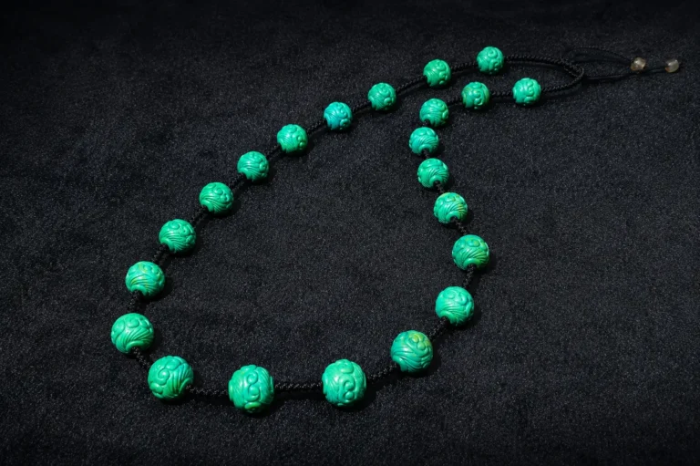 A handmade necklace featuring carved green turquoise beads with natural matrix on a black surface.