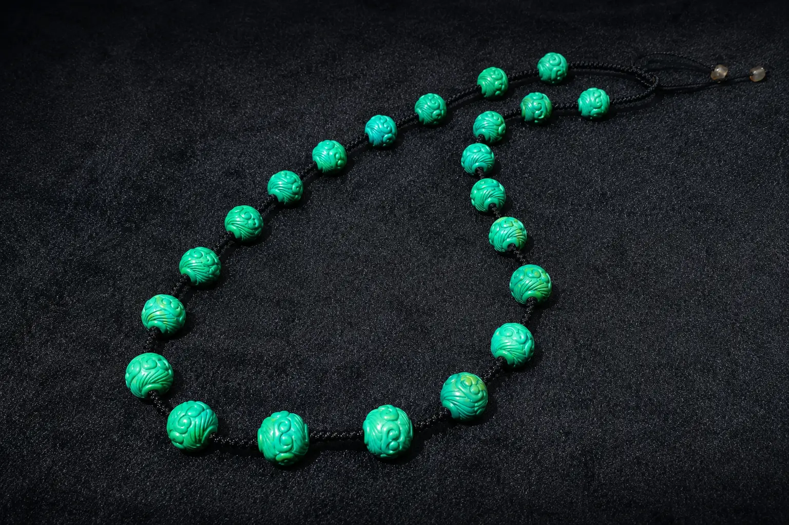 A handmade necklace featuring carved green turquoise beads with natural matrix on a black surface.