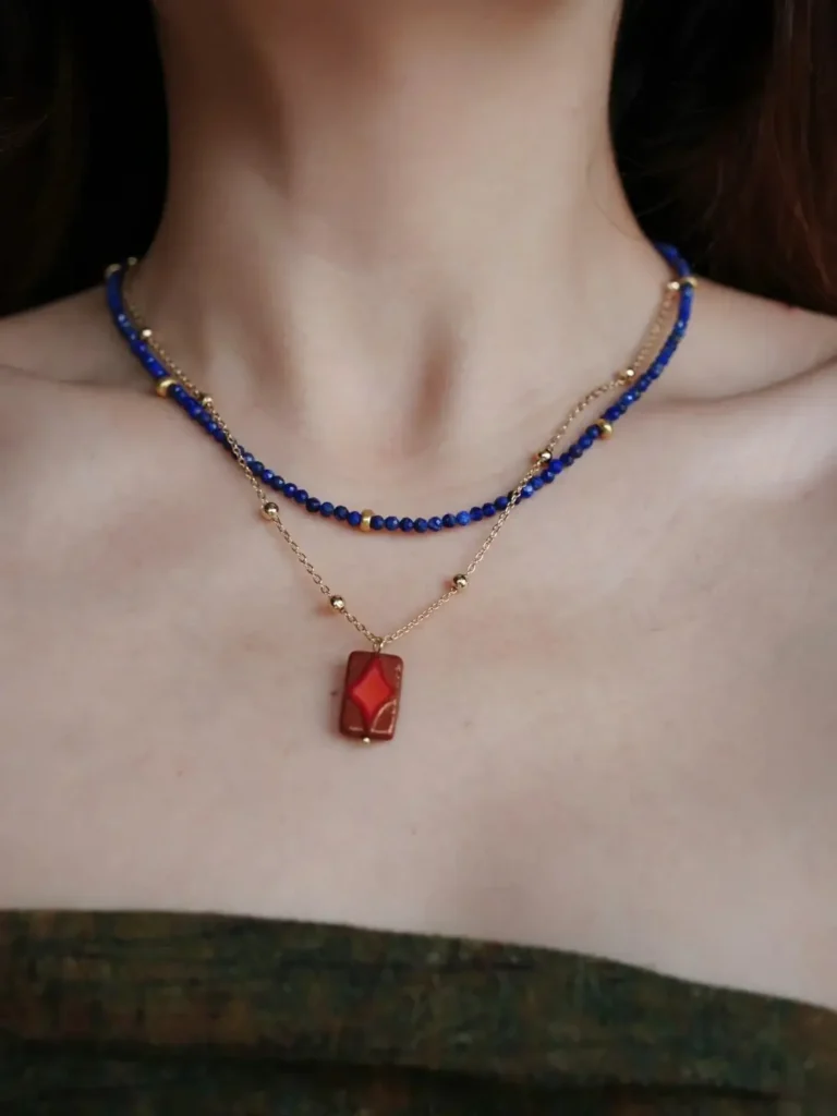 Blue beaded necklace layered with a gold pendant chain, worn with a strapless top.