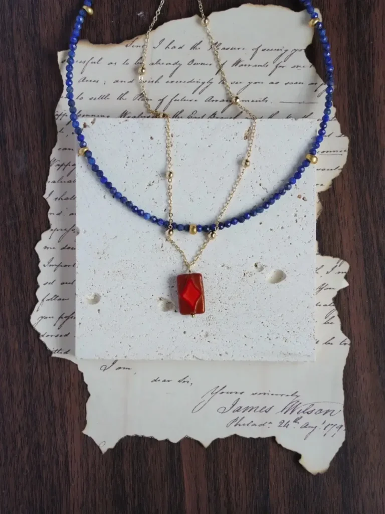 Lapis lazuli beads layered with a gold pendant chain on a jewelry display.
