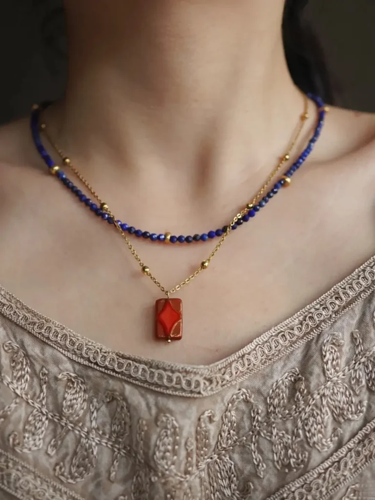 Faceted lapis lazuli beads layered with a gold chain over a scoop neck top.