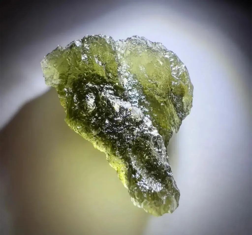 A translucent, olive green raw moldavite specimen featuring deeply etched natural textures.