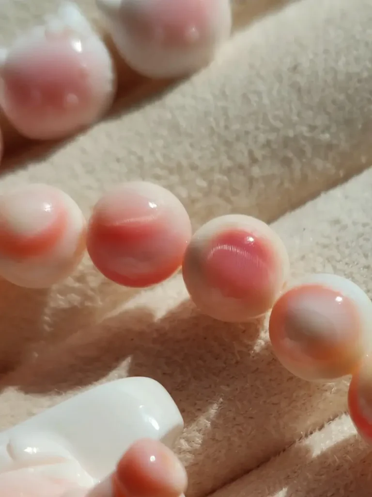 Close-up of polished Queen Conch shell beads showing pink and white spiral patterns.
