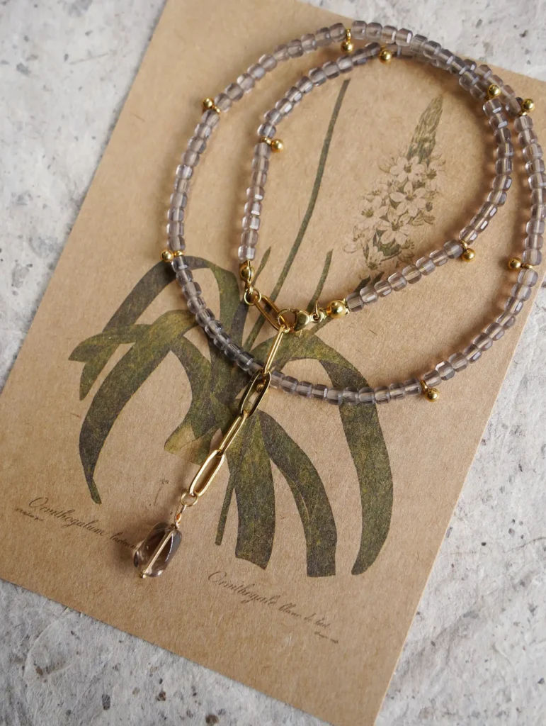 A translucent gray-brown ice obsidian beaded necklace placed on a botanical card.