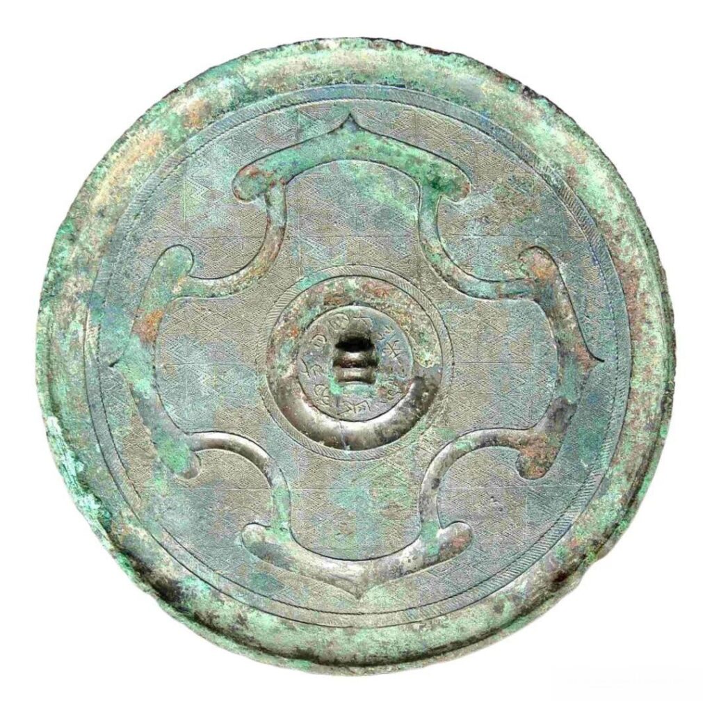 An ancient Chinese circular bronze mirror decorated with a symmetrical four-petal pattern.
