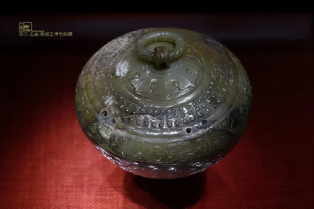 An ancient Chinese circular jade box featuring an intricately carved lid with a central ring.