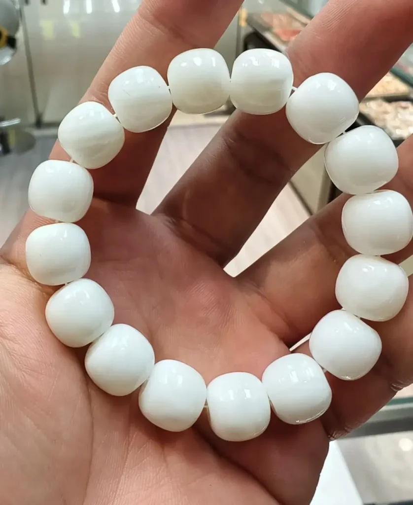 Hand holding a white Tridacna shell bracelet with smooth barrel-shaped beads and pearly luster.
