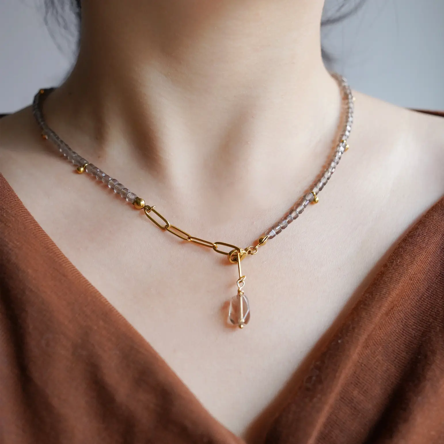 A woman wearing a Y-drop gemstone necklace with a V-neck brown top.