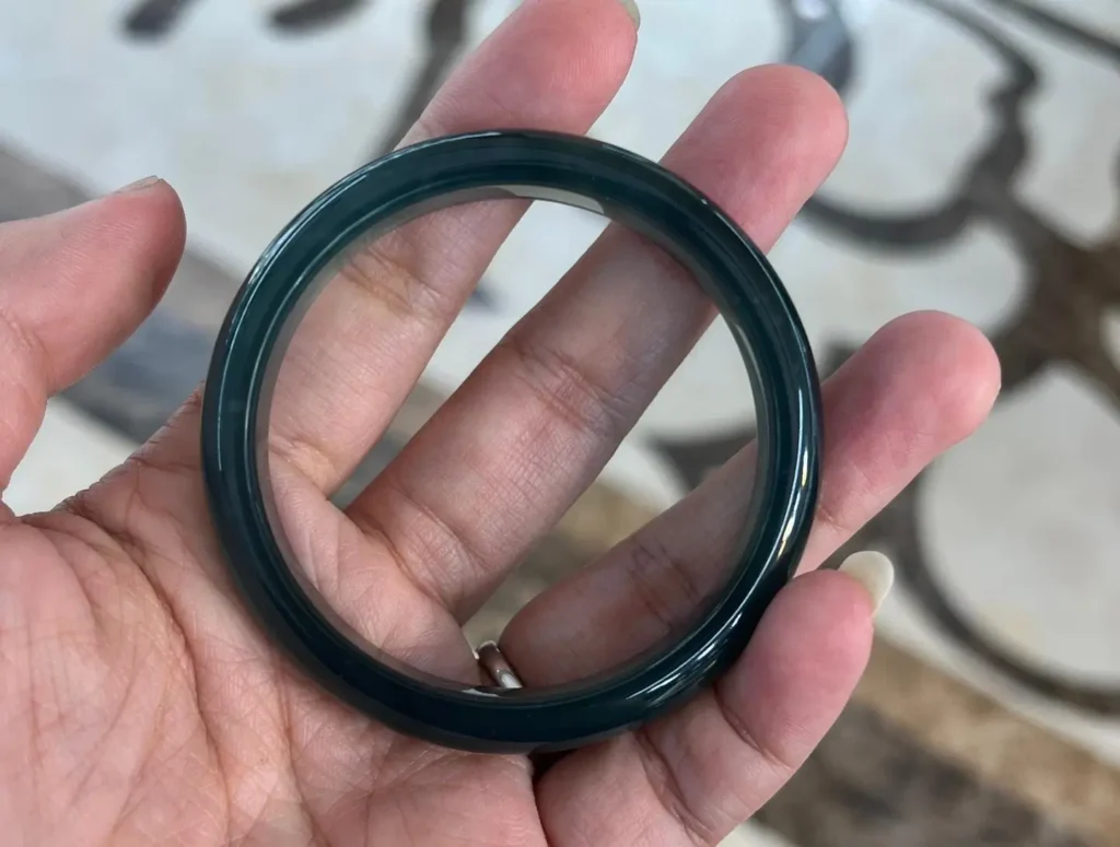 A dark blue-water Guatemalan jadeite bangle held in a hand showing a muted tone.