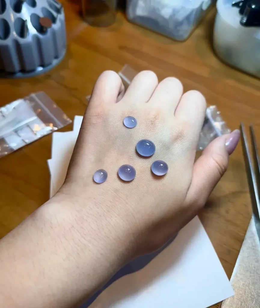 Five purple Guatemalan jadeite cabochons displayed on the back of a hand.