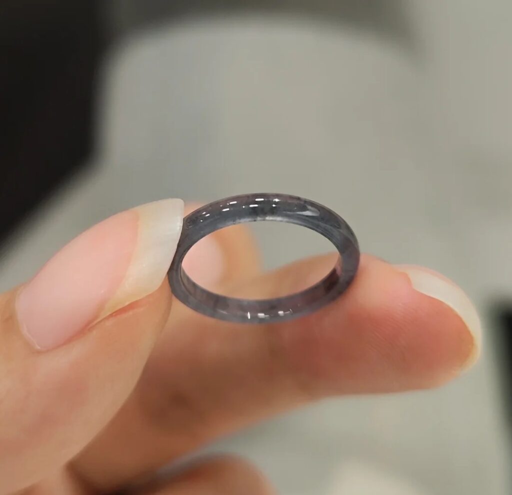 A dark gray ring with translucent texture held between fingertips.