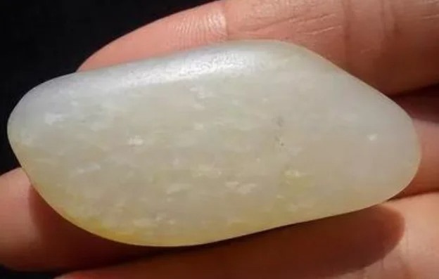 Raw Hetian jade pebble showing scattered white dot-like cotton inclusions inside the stone.